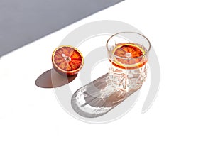 Minimal style creative composition made of half blood red orange and a glass with cocktail on white background with shadow. Summer