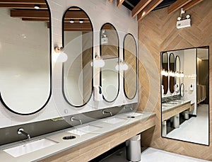 Minimal style and modern beautiful interior design of public restroom with row of mirrors, sinks with faucets, bright decorating