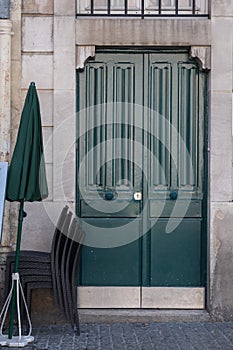 Minimal style wooden door painted in deep green color and closed green parasol nearby.