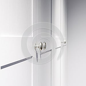 Minimal white closet or wardrobe with silver door handles. Close-up and selective focus at the knob handle.