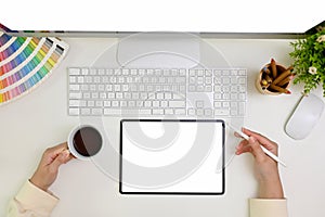 Minimal white workspace top view with a female graphic designer sipping coffee and using tablet