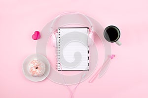 Minimal workplace with white blank notepad, pink headphones, heart, coffee cup and donut on pink background. Top view. Flat lay