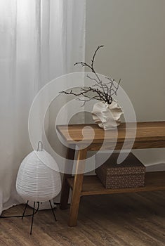 Minimalism scandinavian style interior decor - paper lamp, creative ceramic vase with dry branches on a wooden bench in the living