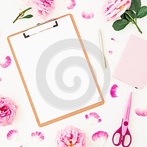 Minimalism workspace with clipboard, pink roses, petals and accessories on white background. Flat lay, top view. Blogger of freela