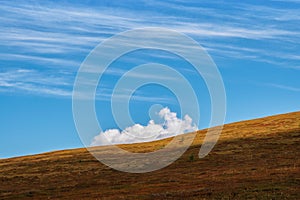 Minimalist alpine landscape with mountain silhouette under blue sky with alone big cloud. Autumn slope mountain and light sky.