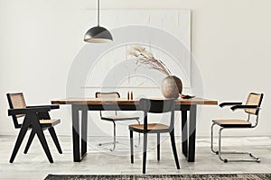 Minimalist composition of dining room interior with wooden table, design chairs, dried flowers in a vase, black pendant lamp, art.