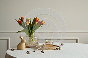 Minimalist composition of easter dining room interior with copy space, round table, vase with tulips, easter bunny sculpture,