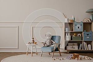 Minimalist composition of kid room interior with copy space, blue armchair, wooden sideboard, beige rug, plush toys, wooden