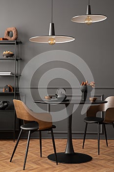 Minimalist composition of living room interior with black round coffee table, stylish chair, wooden sideboard, dark wall with