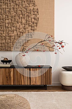 Minimalist composition of living room interior with mock up poster frame, vase with rowan, wooden sideboard, carpet, slippers,