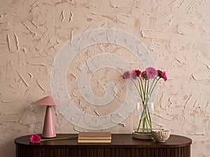 Minimalist composition of living room interior with wooden sideboard, glass vase with pink flowers, lamp, grey casket, books,