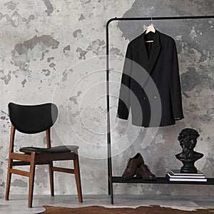 Minimalist compostion at living room interior with concrete wall, chair, hanger with clothes and elegant personal accessories.