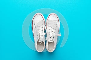 Minimalist flat lay image of white gumshoes over turquoise blue background