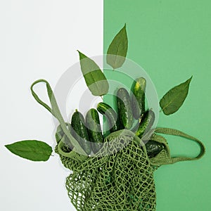 Minimalist fresh scene. Organic cucumber and pumpkin in mesh bag on green and white background. Zero waste, bio market, eco, vegan