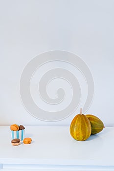 Minimalist Halloween concept - sweets, macarons dessert in a paper cup, and decorative pumpkins. Chocolate and pumpkin