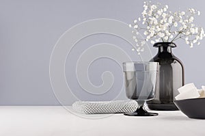 Minimalist interior bathroom in monochrome grey color - black glass vase with small white flowers, goblet, silver cosmetic bag.