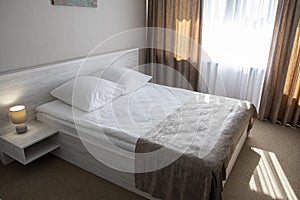 Minimalist interior of the bedroom with a double bed on the wooden floor, CURTAINS ON the WINDOW, sunlight. home interior.