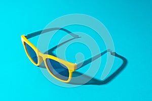 Minimalist photo of stylish yellow sunglasses with harsh shadow as summer concept.