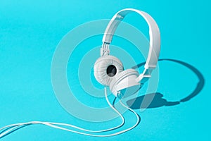 Minimalist photo of white levitating headphones with cable over blue background