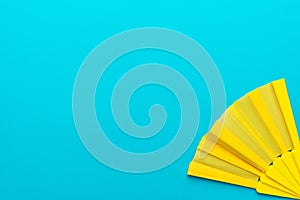 Minimalist photo of yellow hand fan on turquoise blue background with copy space