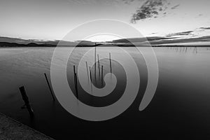 Minimalist view of fishing net poles on a lake, with perfectly still water and empty sky at dusk