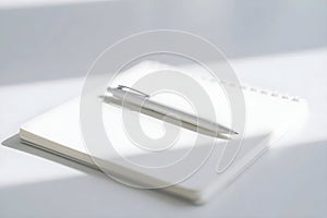 A minimalist white scene featuring a pen resting on top of a closed notebook in soft light setting