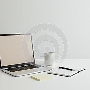 A minimalist workspace featuring a closed silver laptop on a white table,