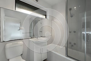 Minimalistic bathroom interior in white and gray tones with a walk-in shower, toilet, and a sink