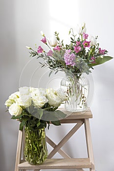 A minimalistic bouquet of white tulips, pink eustoma, hyacinth, eucalyptus in a fluted glass vase on a white panel of an