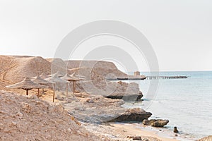 Minimalistic calm travel background with lonely small house and the ruined pier. Sandy and rocky coast in Egypt