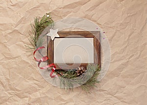 Minimalistic christmas composition. Wooden photo frame on craft paper background with Christmas tree branches, decorations, pine