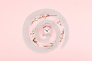 Minimalistic  Flat lay, top view composition with pink alarm clock and blossom cherry flower branch on pink background. Trendy