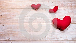 Minimalistic greeting card as gift for Valentines day holiday. Three red toy soft plush hearts on wooden table. Flat background