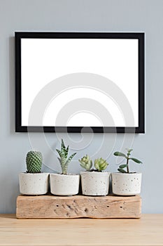Minimalistic home interior with mock up photo frame on the brown table with composition of cacti and succulents.
