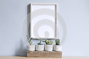 Minimalistic home interior with mock up photo frame on the brown table with composition of cacti and succulents.