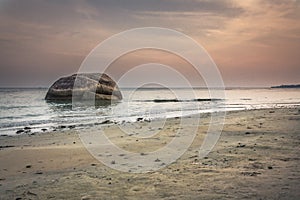 Minimalistic landscape at tropical beach during sunset with big round stone in water