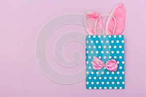 Minimalistic pastel image with blue gift bag with Easter bunny ears and the bow tie on pink background with copy space