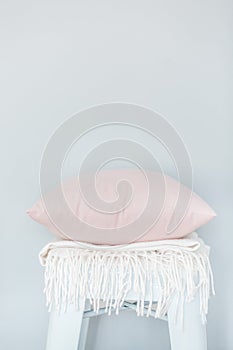Minimalistic skandinavian picture of a light pink pillow and a white plaid on the chair near a pale blue wall photo