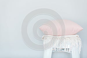 Minimalistic skandinavian picture of a light pink pillow and a white plaid on the chair near a pale blue wall photo