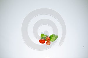 Minimalistic top view of fresh basil leafs with a rond cherry tomato and a sliced open cherry tomato isolated on a white