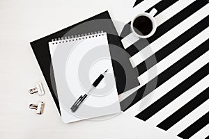 Minimalistic workspace with book, notebook, pencil, cup of coffee on striped black and white background. Flat lay style Top view