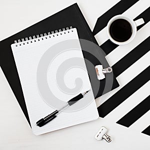 Minimalistic workspace with book, notebook, pencil, cup of coffee on striped black and white background. Flat lay style Top view