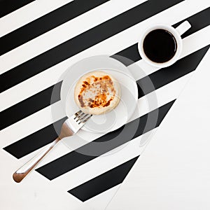 Minimalistic workspace with cup of coffee, bakery, isolated on striped black and white background. Flat lay style Top view.