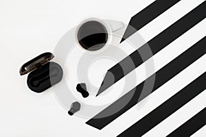 Minimalistic workspace with cup of coffee, wireless earphones on striped black and white background. Flat lay style Top view.