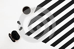 Minimalistic workspace with cup of coffee, wireless earphones on striped black and white background. Flat lay style Top view.