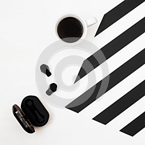 Minimalistic workspace with cup of coffee, wireless earphones on striped black and white background. Flat lay style Top view.