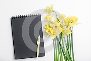 Minimalistic workspace. white work desk with notepad black paper, pen and bouquet flower.