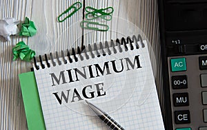MINIMUM WAGE - words on a white notepad on the background of a calculator, paper clips