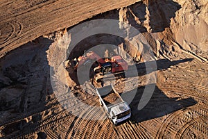 Mining excavator load the sand into dump truck in open pit. Developing the sand in the opencast. Heavy machinery on earthworks in