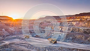 A mining site with large dump trucks under a setting sun